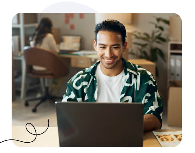 A man focused on his laptop screen while working in a modern office setting.